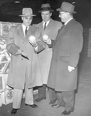 Egan stands between two unidentified men, likely buyers, at a New York City produce market in the mid-1940s