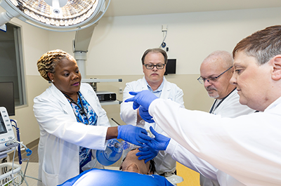 Nursing students practice with instructors in a simulated operating room, learning procedures they will use on real patients.