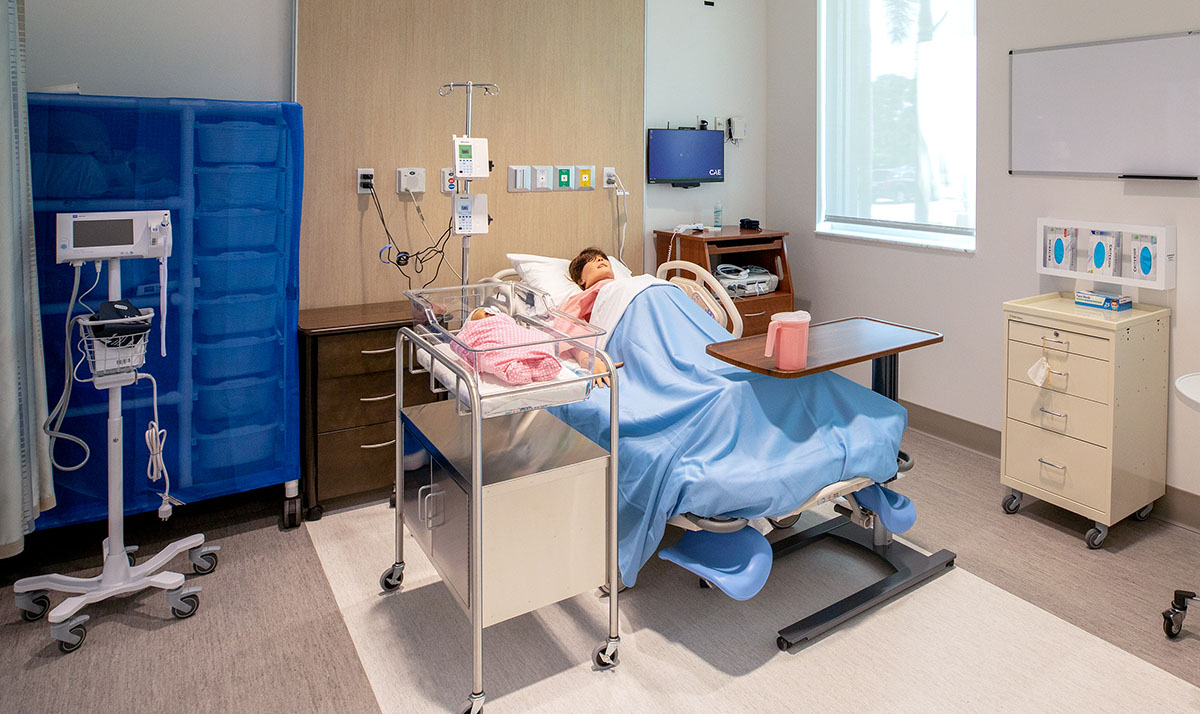 A simulated pregnant patient lies in a room with an infant mannequin. Both contain advanced electronics enabling them to act like real humans. 